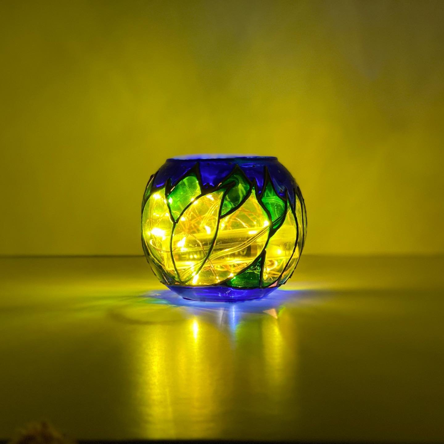 Glowing painted glass votive with green leaves on cobalt — Glass Art Lab studio